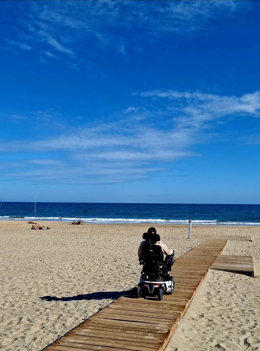 Anthony en fauteuil sur un chemin accessible menant à la plage